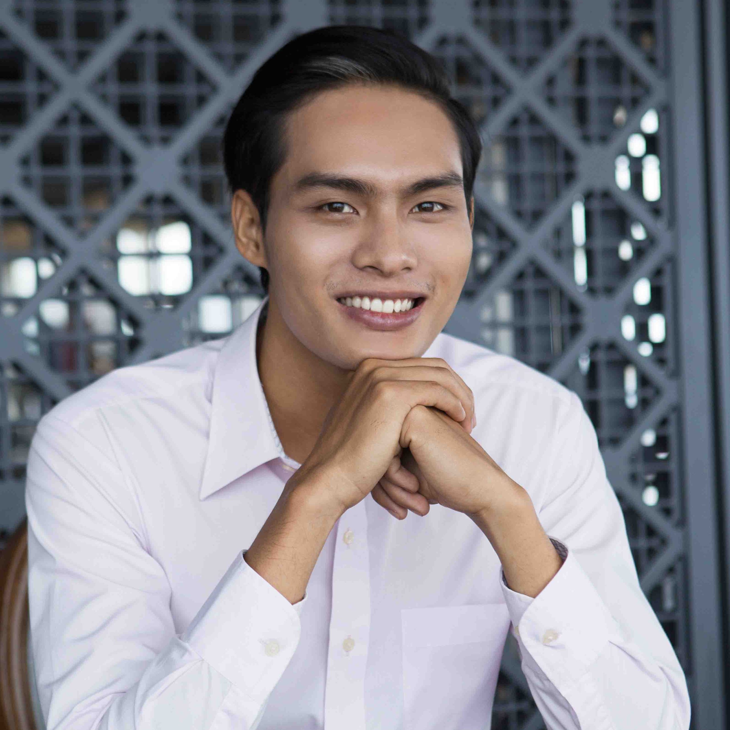 Portrait of happy young Asian businessman with hands under chin sitting in restaurant and smiling at camera